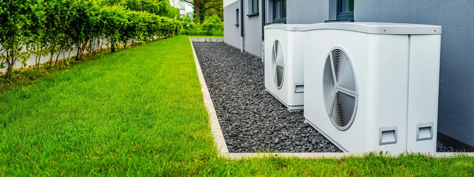 Dos bombas de calor de aerotermia instaladas en el exterior de una vivienda con jardín